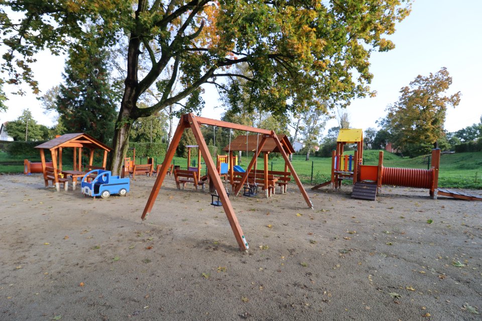 Plac zabaw. Na zdjęciu w centrum widać huśtawki dwie, dalej elementy zabawowo-rekreacyjne. 